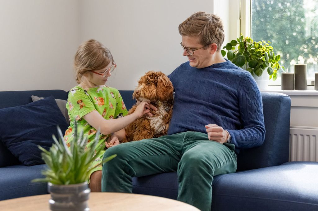 Far og datter sidder i sofa med deres australske labradoodle