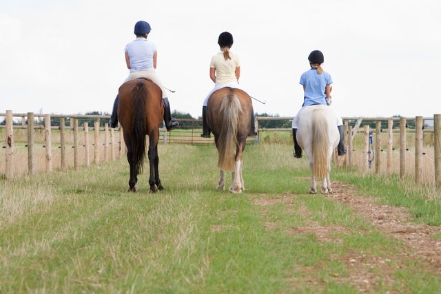 Tre ponyryttere ses bagfra på en mark