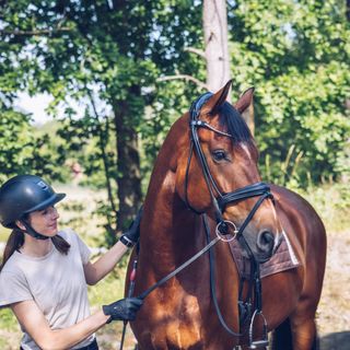 Kvinde står med sin hest i skoven på en ridetur