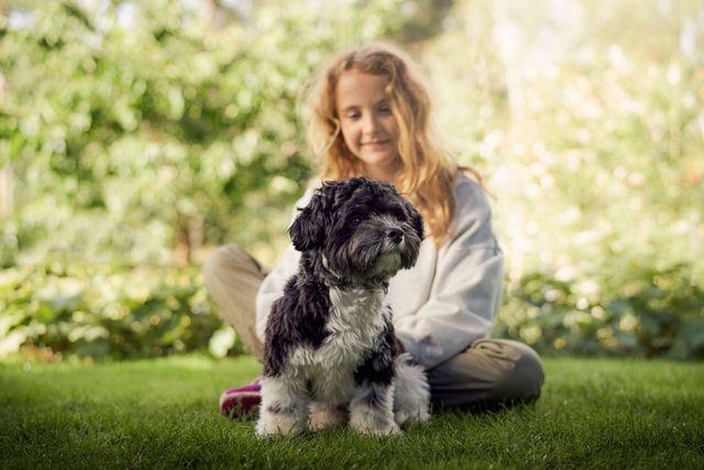 Pige sidder ude på græsplænen med sin hund foran sig.
