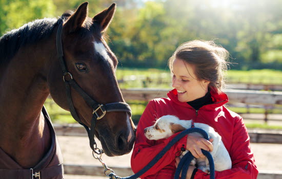 Pige står med sin hest og hund