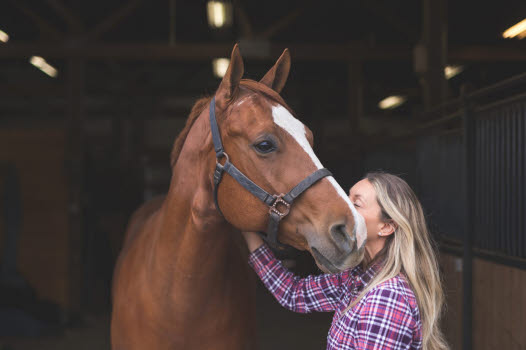 Kvinde kysser hest i stalden.
