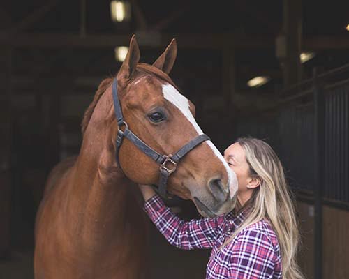 Kvinde kysser hest i stalden.