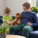 Far og datter sidder i sofa med deres australske labradoodle