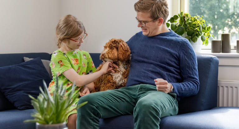 Far og datter sidder i sofa med deres australske labradoodle
